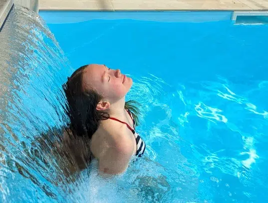 Jeune fille profitant de la cascade d’eau dans la piscine chauffée du camping à Agon-Coutainville dans la Manche