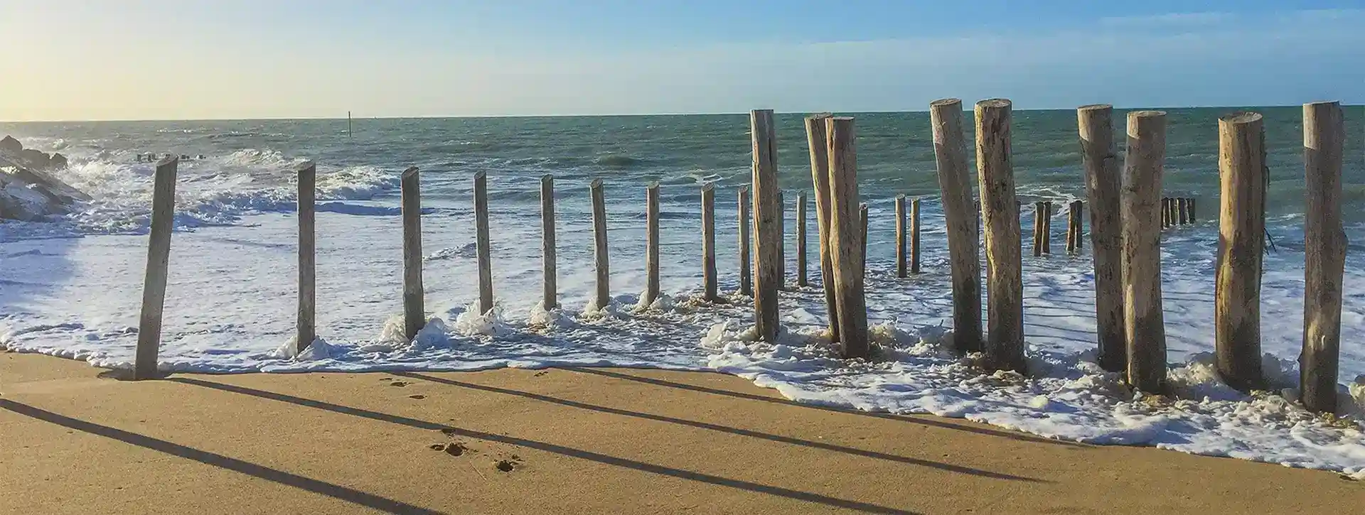 Plage d’Agon-Coutainville avec les vagues et les pieux en bois, proche du camping dans la Manche.