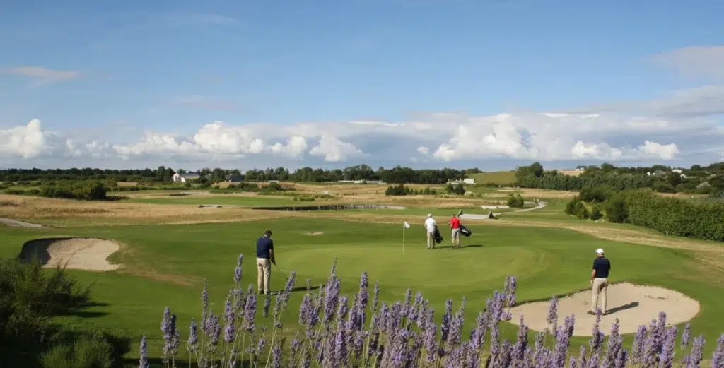 Vue du golf d’Agon-Coutainville avec green, bunkers de sable, joueurs sur le parcours et paysage normand en arrière-plan